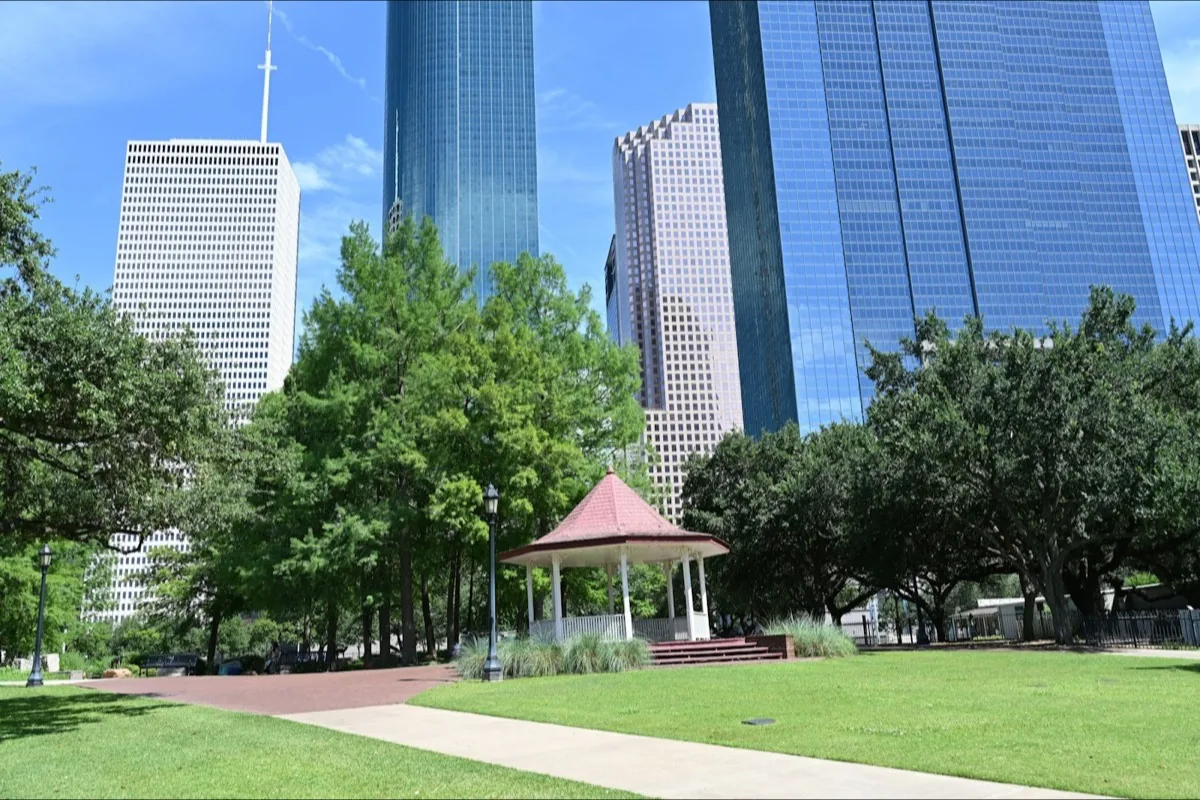 Downtown Houston buildings behind trees and a park pavilion