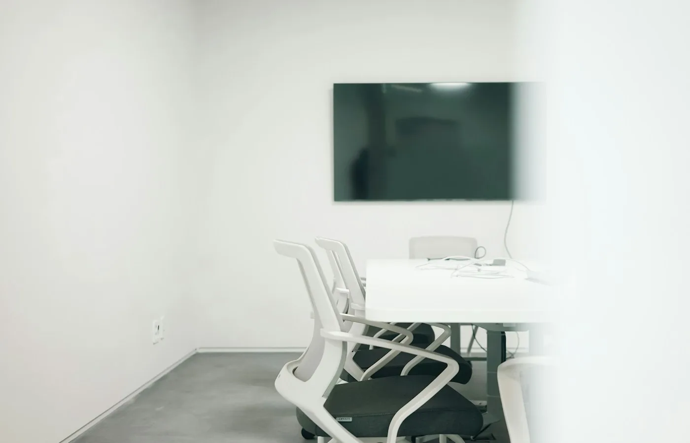 Bright contemporary meeting room with white mesh chairs and a wall-mounted display